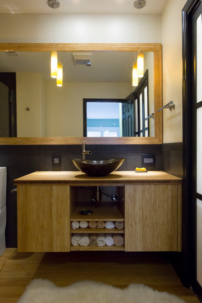 Пример оригинального дизайна: главная ванная комната среднего размера в современном стиле с настольной раковиной, светлыми деревянными фасадами, столешницей из дерева, душем без бортиков, раздельным унитазом, керамогранитной плиткой, желтыми стенами, полом из бамбука, плоскими фасадами, черной плиткой, желтым полом, душем с распашными дверями и желтой столешницей