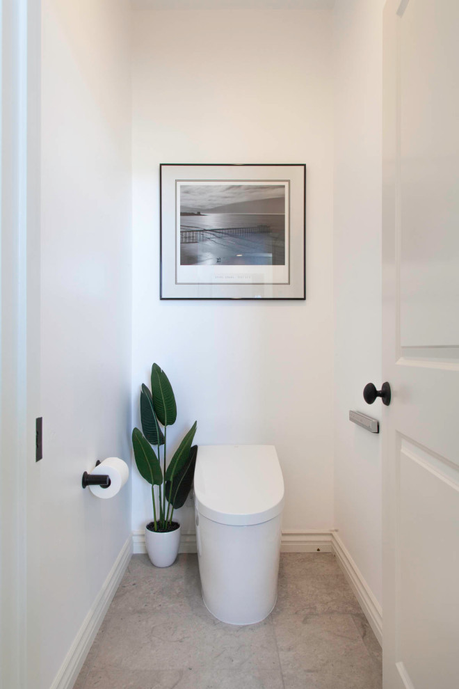 Exemple d'un grand WC et toilettes bord de mer en bois vieilli avec un placard avec porte à panneau encastré, WC séparés, un carrelage blanc, un mur blanc, un sol en calcaire, un lavabo encastré, un plan de toilette en quartz, un sol gris et un plan de toilette gris.
