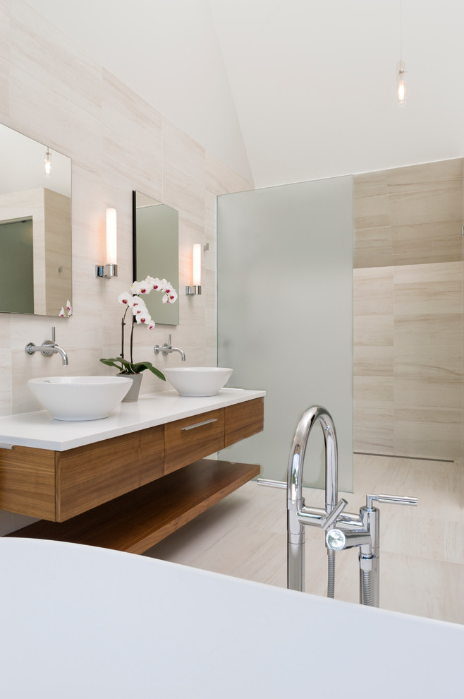 Bild på ett mellanstort funkis vit vitt en-suite badrum, med ett fristående handfat, släta luckor, skåp i mellenmörkt trä, bänkskiva i kvarts, beige kakel, stenkakel, ett fristående badkar, våtrum, beiget golv och med dusch som är öppen