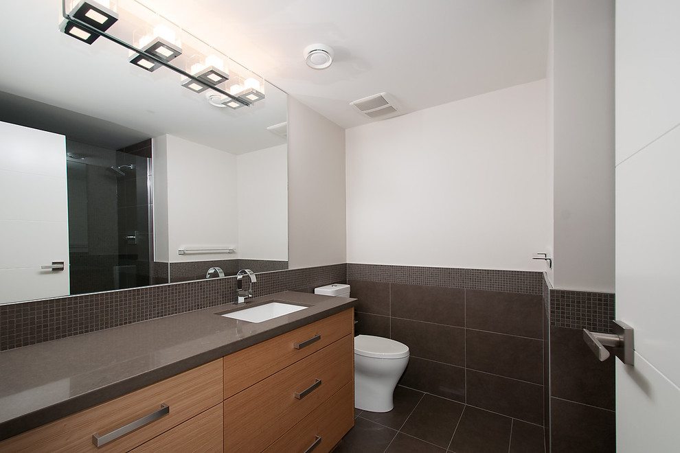 Exemple d'une très grande salle de bain principale moderne en bois foncé avec un lavabo encastré, un placard à porte plane, un plan de toilette en surface solide, une baignoire en alcôve, un combiné douche/baignoire, WC à poser, un carrelage gris et un mur gris.