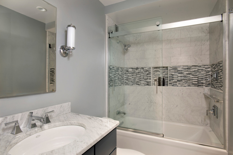 Photo of a small traditional ensuite bathroom in Boston with shaker cabinets, blue cabinets, an alcove bath, a shower/bath combination, a two-piece toilet, grey tiles, stone tiles, grey walls, marble flooring, a submerged sink and marble worktops.