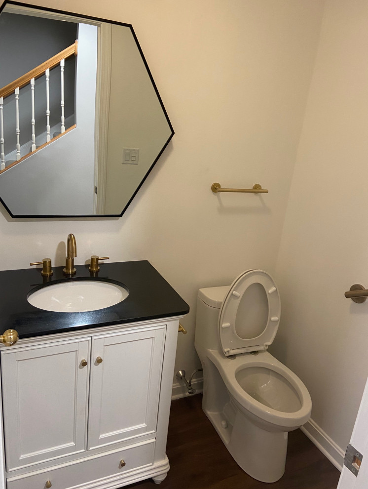 Cette image montre une petite salle de bain design avec un placard à porte shaker, des portes de placard blanches, sol en stratifié, un sol marron, WC à poser, un mur blanc, un lavabo posé, un plan de toilette en granite et un plan de toilette noir.