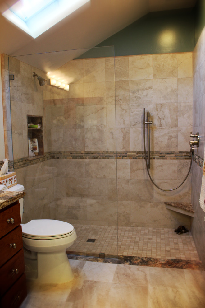 Inredning av ett amerikanskt badrum, med ett undermonterad handfat, luckor med upphöjd panel, skåp i mörkt trä, granitbänkskiva, en dusch i en alkov, en toalettstol med hel cisternkåpa, brun kakel och stenkakel