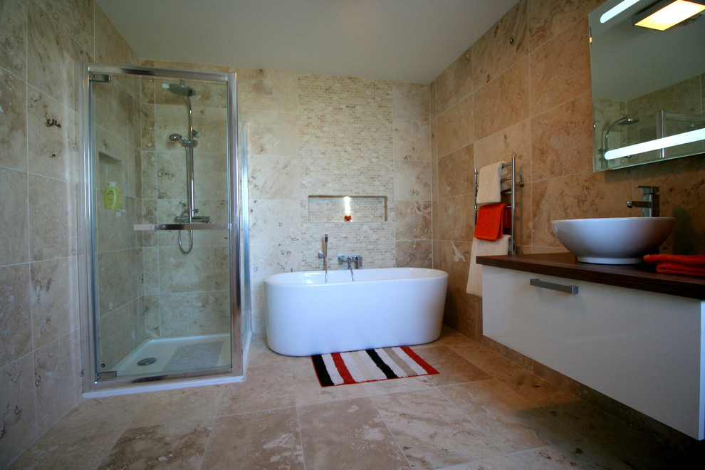 Inspiration for a large modern shower room bathroom in Dublin with an integrated sink, flat-panel cabinets, medium wood cabinets, wooden worktops, a freestanding bath, a corner shower, a one-piece toilet, beige tiles, stone tiles, beige walls and travertine flooring.