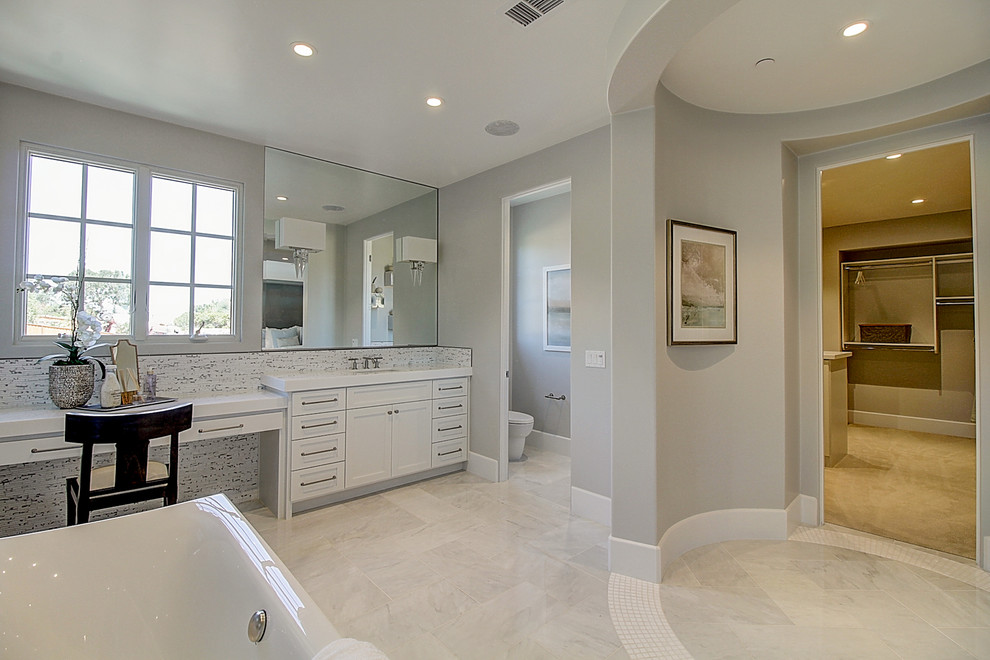 На фото: большая главная ванная комната с фасадами в стиле шейкер, белыми фасадами, отдельно стоящей ванной, душем без бортиков, раздельным унитазом, полом из керамогранита, накладной раковиной и душем с распашными дверями с