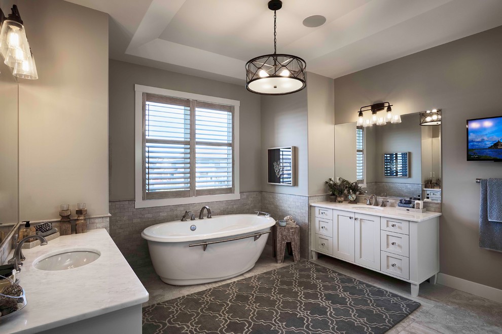 Inspiration for a large coastal ensuite bathroom in Calgary with a submerged sink, recessed-panel cabinets, white cabinets, marble worktops, a freestanding bath, a built-in shower, a one-piece toilet, grey tiles, ceramic tiles, grey walls and ceramic flooring.