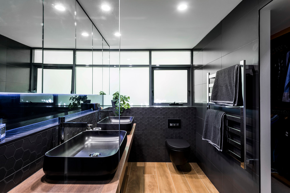 Medium sized modern ensuite bathroom in Brisbane with freestanding cabinets, black cabinets, a built-in shower, a wall mounted toilet, black tiles, ceramic tiles, black walls, ceramic flooring, a vessel sink and laminate worktops.