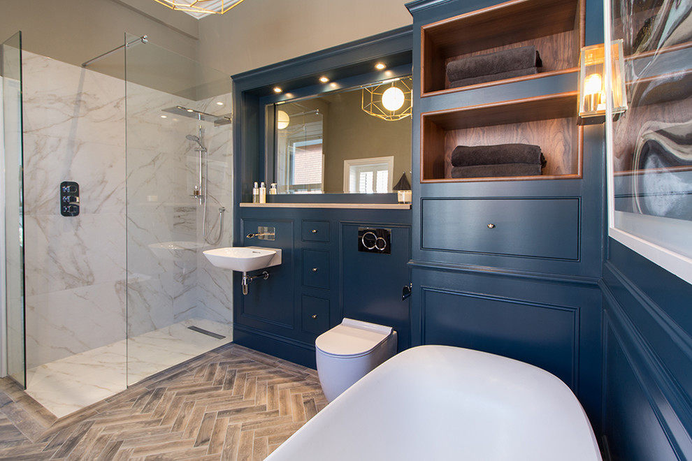 This is an example of a large contemporary ensuite wet room bathroom in Dublin with recessed-panel cabinets, blue cabinets, a freestanding bath, a wall mounted toilet, beige tiles, porcelain tiles, blue walls, porcelain flooring, a wall-mounted sink, engineered stone worktops, brown floors and an open shower.