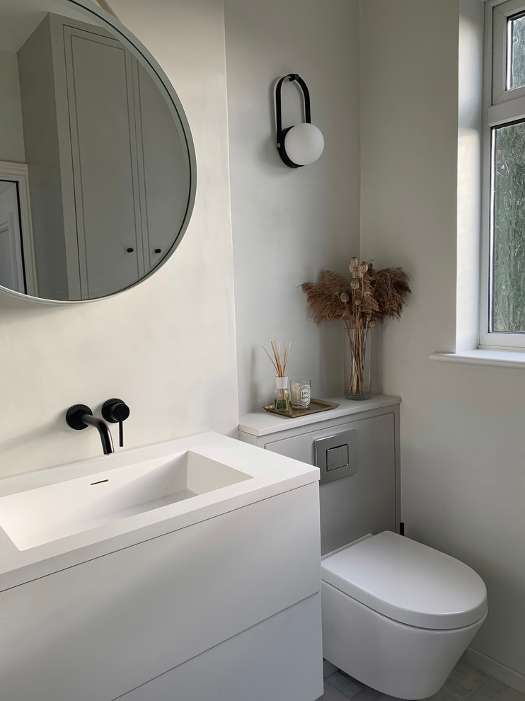 Inspiration for a small contemporary shower room bathroom in London with flat-panel cabinets, white cabinets, a built-in bath, a wall mounted toilet, grey tiles, grey walls, marble flooring, a wall-mounted sink, solid surface worktops, white floors, a hinged door and white worktops.