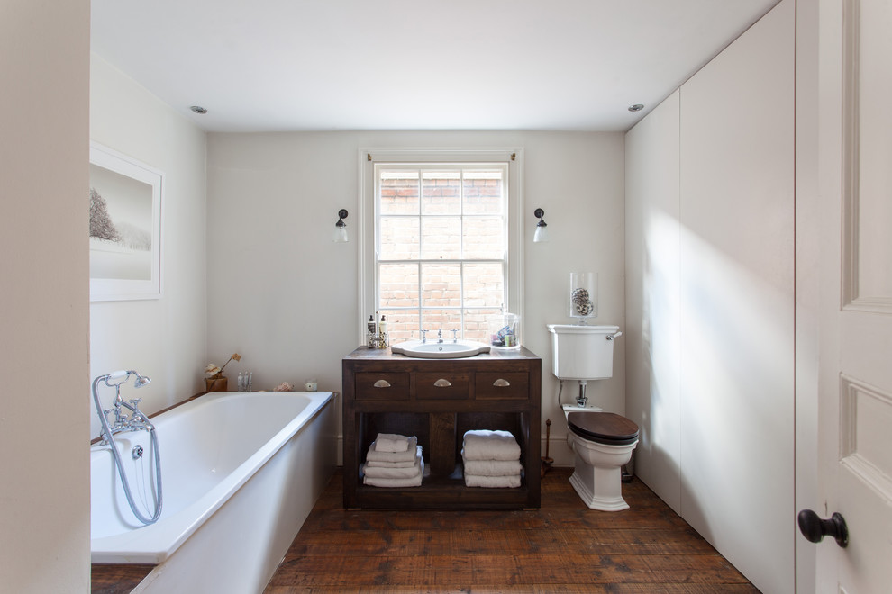 Bild på ett mellanstort vintage brun brunt badrum, med släta luckor, skåp i mörkt trä, ett platsbyggt badkar, en dusch/badkar-kombination, en toalettstol med separat cisternkåpa, vita väggar, mellanmörkt trägolv, ett nedsänkt handfat, träbänkskiva, brunt golv och med dusch som är öppen