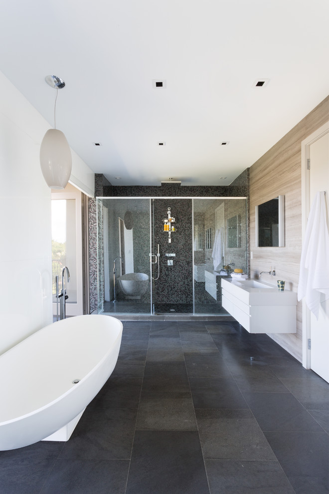 Großes Modernes Badezimmer En Suite mit freistehender Badewanne, flächenbündigen Schrankfronten, weißen Schränken, Duschnische, weißer Wandfarbe, integriertem Waschbecken, Mineralwerkstoff-Waschtisch, Schieferfliesen und Steinwänden in Miami