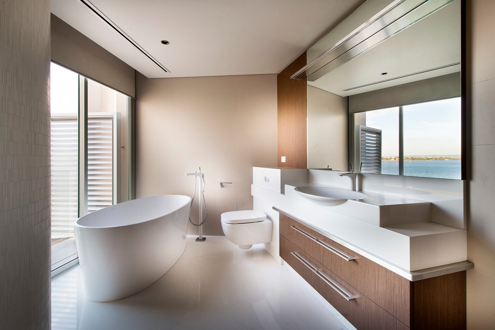 Modelo de cuarto de baño contemporáneo con armarios con paneles lisos, bañera exenta, sanitario de pared, paredes beige y encimeras blancas