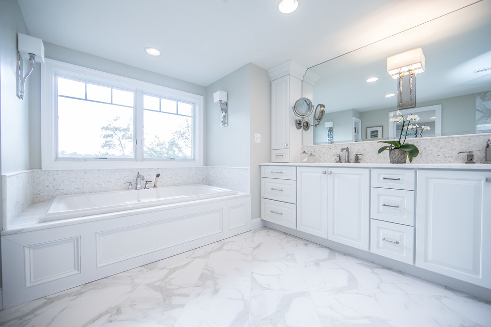 Photo of a large traditional ensuite bathroom in DC Metro with raised-panel cabinets, white cabinets, a built-in bath, white tiles, stone tiles, grey walls, marble flooring, a submerged sink and marble worktops.