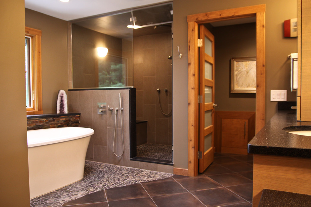 Источник вдохновения для домашнего уюта: большая главная ванная комната в стиле фьюжн с врезной раковиной, светлыми деревянными фасадами, столешницей из искусственного кварца, отдельно стоящей ванной, двойным душем, серой плиткой, керамогранитной плиткой, серыми стенами, полом из галечной плитки, коричневым полом и душем с распашными дверями