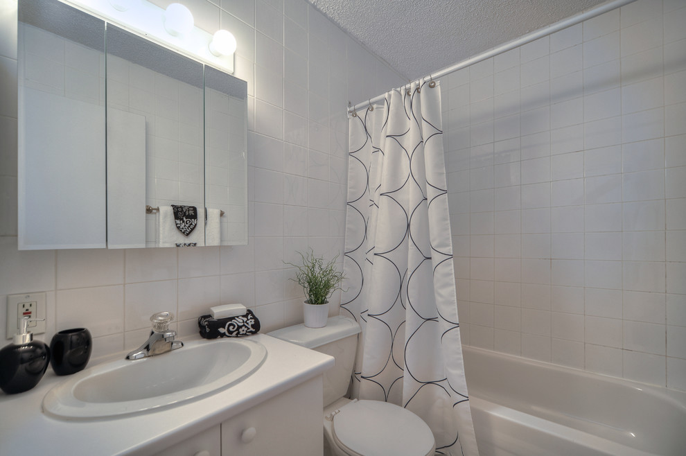 Inredning av ett modernt litet en-suite badrum, med ett nedsänkt handfat, släta luckor, vita skåp, laminatbänkskiva, ett badkar i en alkov, en dusch/badkar-kombination, en toalettstol med separat cisternkåpa, vit kakel, keramikplattor, vita väggar och klinkergolv i keramik
