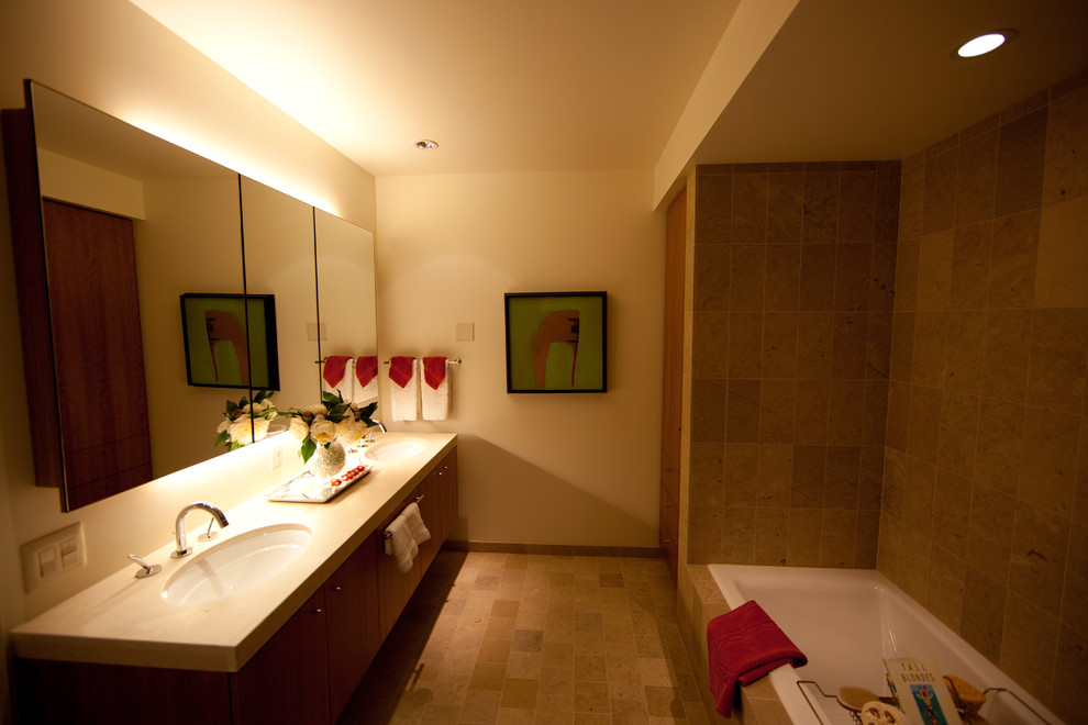 Cette image montre une salle de bain principale design en bois foncé de taille moyenne avec un placard à porte plane, une baignoire posée, un carrelage beige, un carrelage de pierre, un mur jaune, tomettes au sol, un lavabo encastré et un plan de toilette en surface solide.