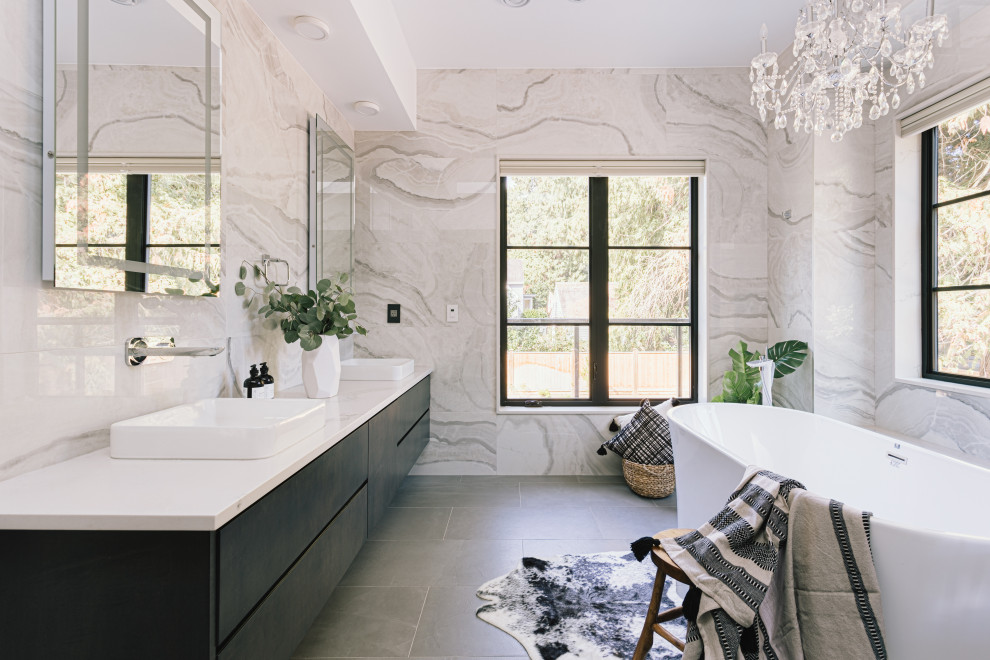 Идея дизайна: главная ванная комната среднего размера в стиле модернизм с фасадами с выступающей филенкой, белыми фасадами, отдельно стоящей ванной, душем над ванной, унитазом-моноблоком, серой плиткой, керамической плиткой, белыми стенами, полом из керамогранита, настольной раковиной, столешницей из гранита, серым полом, душем с распашными дверями и белой столешницей