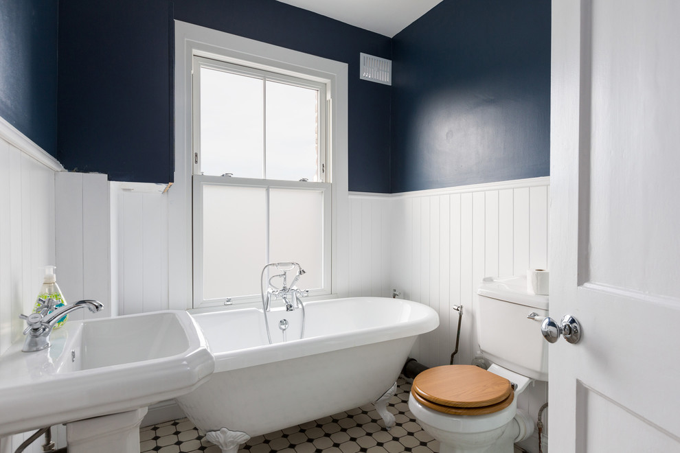 Cette photo montre une salle de bain chic de taille moyenne pour enfant avec une baignoire sur pieds, WC séparés, un combiné douche/baignoire, un mur bleu, un lavabo de ferme et un sol blanc.
