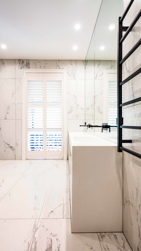 Modern inredning av ett en-suite badrum, med släta luckor, vita skåp, vit kakel, marmorkakel, marmorgolv, ett integrerad handfat, bänkskiva i akrylsten och vitt golv