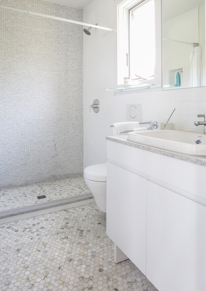 Bild på ett mellanstort funkis vit vitt en-suite badrum, med släta luckor, vita skåp, ett platsbyggt badkar, en dusch i en alkov, en toalettstol med hel cisternkåpa, vit kakel, mosaik, grå väggar, ett undermonterad handfat, marmorbänkskiva och dusch med gångjärnsdörr