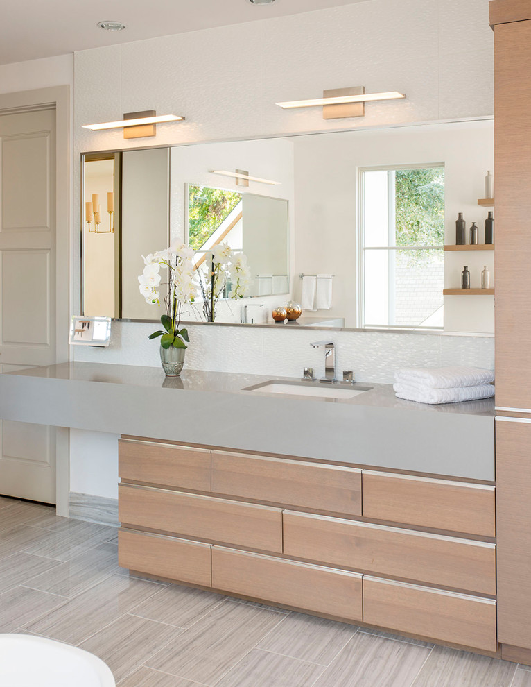Inspiration for a medium sized traditional ensuite bathroom in Dallas with flat-panel cabinets, light wood cabinets, a freestanding bath, white tiles, porcelain tiles, white walls, porcelain flooring, a submerged sink, solid surface worktops, grey floors, an alcove shower and a hinged door.