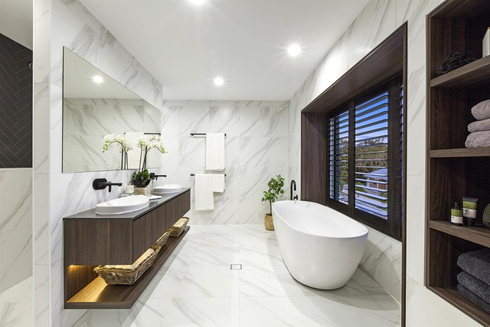 Aménagement d'une salle de bain contemporaine en bois foncé avec un placard à porte plane, une baignoire indépendante, un carrelage blanc, une vasque, un sol blanc, un plan de toilette gris, meuble double vasque et meuble-lavabo suspendu.