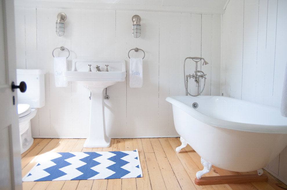 Inspiration for a medium sized coastal ensuite bathroom in Other with a claw-foot bath, a two-piece toilet, white walls, light hardwood flooring and a pedestal sink.