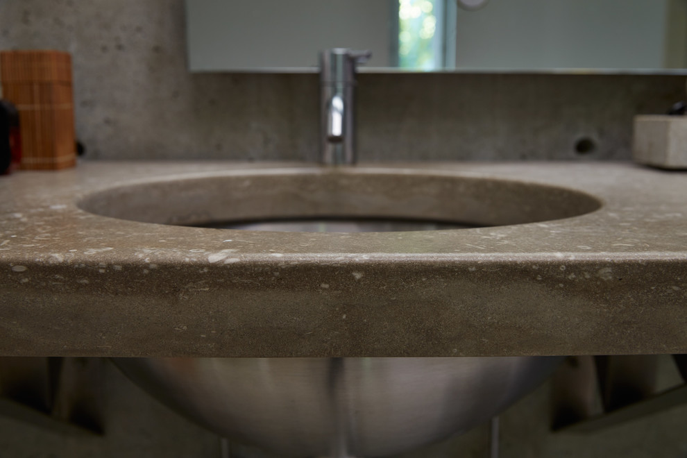 Industriell inredning av ett mellanstort badrum med dusch, med öppna hyllor, en toalettstol med separat cisternkåpa, grå kakel, cementkakel, grå väggar, klinkergolv i keramik, ett undermonterad handfat, bänkskiva i betong och beiget golv