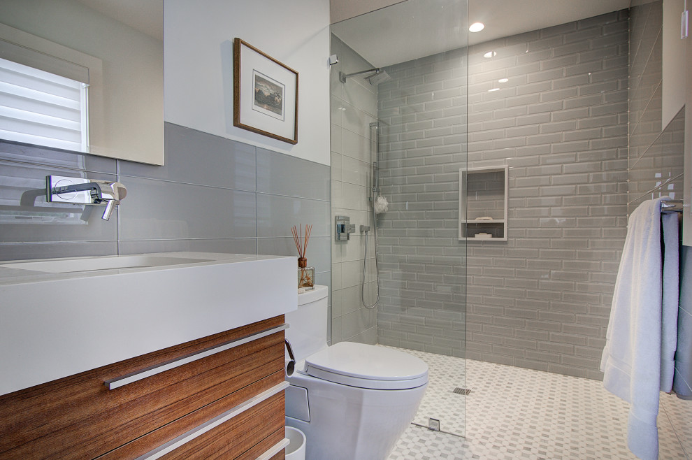 Inredning av ett modernt litet vit vitt en-suite badrum, med släta luckor, bruna skåp, en kantlös dusch, en toalettstol med hel cisternkåpa, grå kakel, glaskakel, grå väggar, marmorgolv, ett undermonterad handfat, bänkskiva i kvartsit, flerfärgat golv och med dusch som är öppen