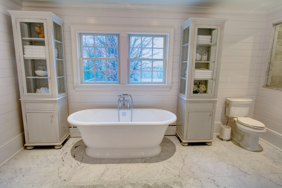 Cette image montre une grande salle de bain principale traditionnelle avec un lavabo encastré, un placard à porte affleurante, des portes de placard grises, un plan de toilette en marbre, une baignoire indépendante, une douche ouverte, WC séparés, un carrelage blanc, un carrelage de pierre, un mur blanc et un sol en marbre.
