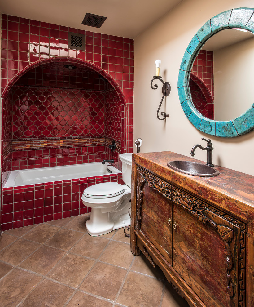 Réalisation d'une salle d'eau sud-ouest américain en bois foncé avec un placard à porte plane, une baignoire en alcôve, un combiné douche/baignoire, WC séparés, un carrelage rouge, un mur beige, un lavabo posé, un plan de toilette en bois et un sol beige.