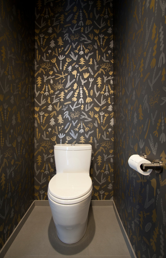 Cette image montre un petit WC et toilettes vintage en bois brun avec un placard à porte plane, WC à poser, un carrelage gris, des carreaux de porcelaine, un mur gris, un sol en carrelage de porcelaine, un lavabo encastré, un plan de toilette en marbre et un sol gris.