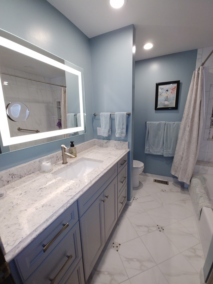 Inspiration for a small classic ensuite bathroom in St Louis with recessed-panel cabinets, grey cabinets, a built-in bath, a shower/bath combination, a one-piece toilet, white tiles, ceramic tiles, blue walls, ceramic flooring, a submerged sink, engineered stone worktops, white floors, a shower curtain and multi-coloured worktops.
