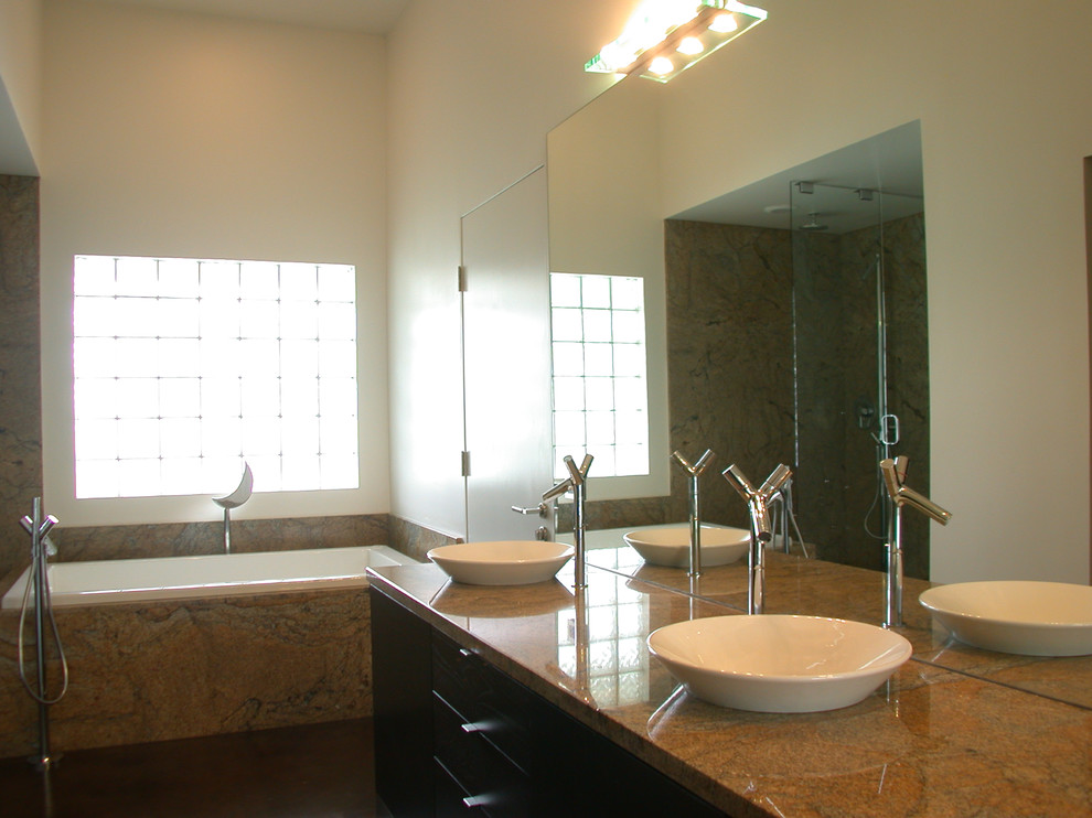 Modelo de cuarto de baño principal moderno de tamaño medio con armarios con paneles lisos, puertas de armario de madera en tonos medios, bañera encastrada, ducha empotrada, paredes blancas, lavabo sobreencimera y encimera de granito