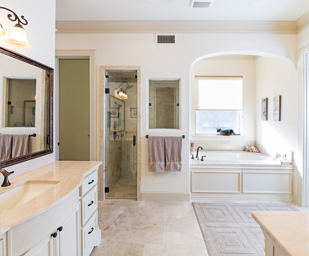 Inspiration for a large classic bathroom in Dallas with a built-in shower, a submerged sink, recessed-panel cabinets, white cabinets, a submerged bath, a two-piece toilet, beige tiles, stone tiles, beige walls and limestone flooring.