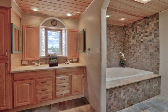 Cette image montre une salle de bain principale sud-ouest américain en bois clair de taille moyenne avec une baignoire posée, un carrelage gris, un carrelage multicolore, mosaïque, un mur beige, un sol en carrelage de porcelaine, un lavabo encastré et un sol gris.