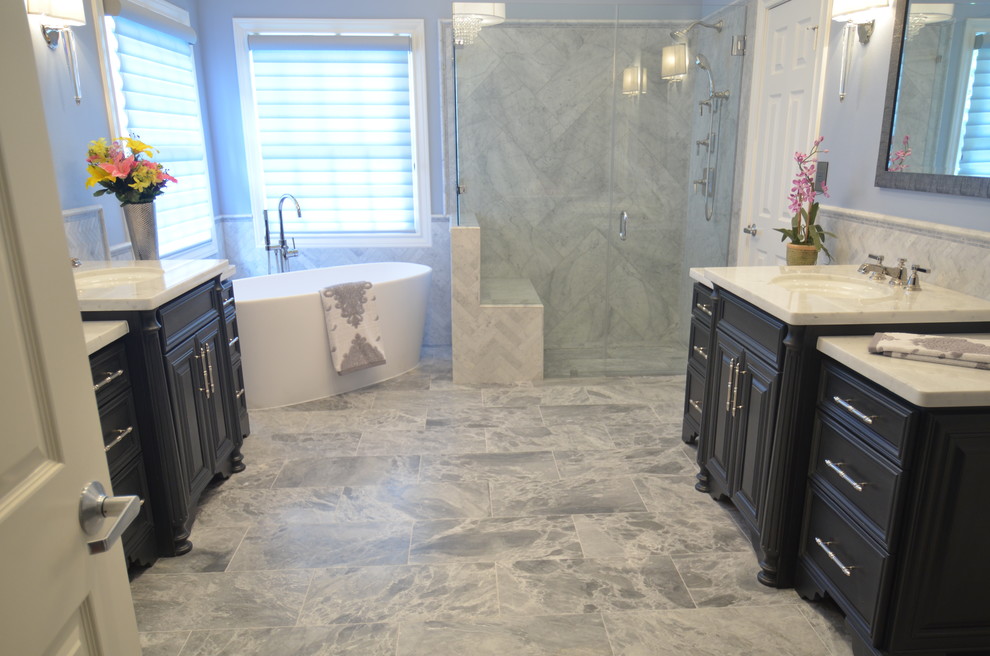 Inredning av ett klassiskt stort en-suite badrum, med möbel-liknande, grå skåp, ett fristående badkar, en kantlös dusch, en toalettstol med separat cisternkåpa, grå kakel, stenkakel, blå väggar, marmorgolv, ett undermonterad handfat och marmorbänkskiva
