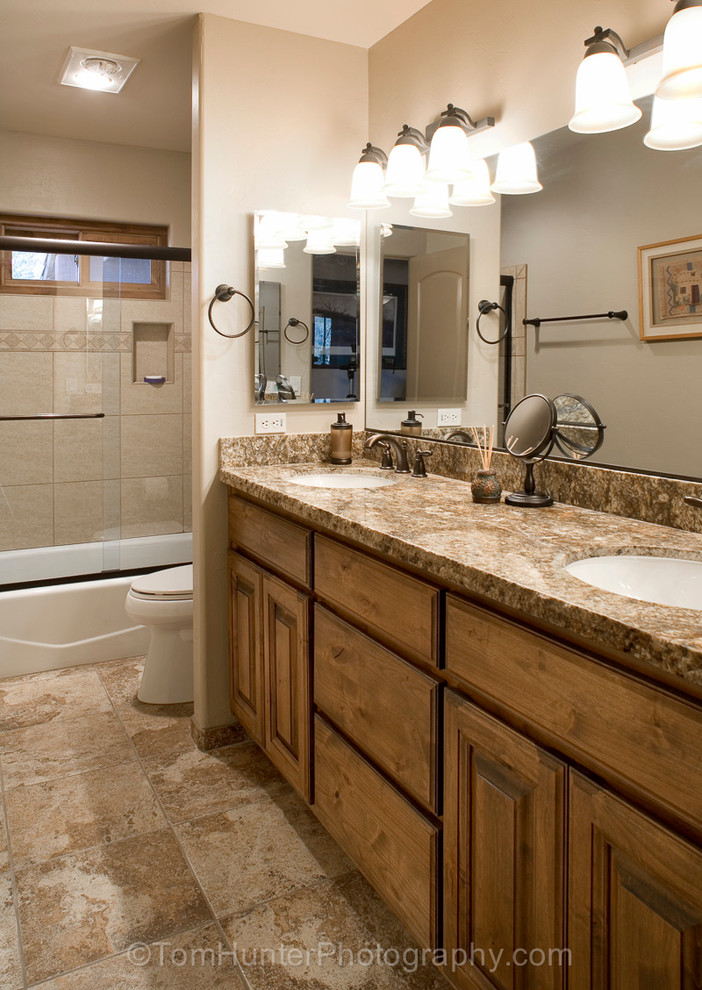 Foto på ett mellanstort amerikanskt badrum, med ett nedsänkt handfat, möbel-liknande, skåp i mellenmörkt trä, marmorbänkskiva, ett platsbyggt badkar, en dusch/badkar-kombination, en toalettstol med hel cisternkåpa, beige kakel, stenkakel, beige väggar och marmorgolv