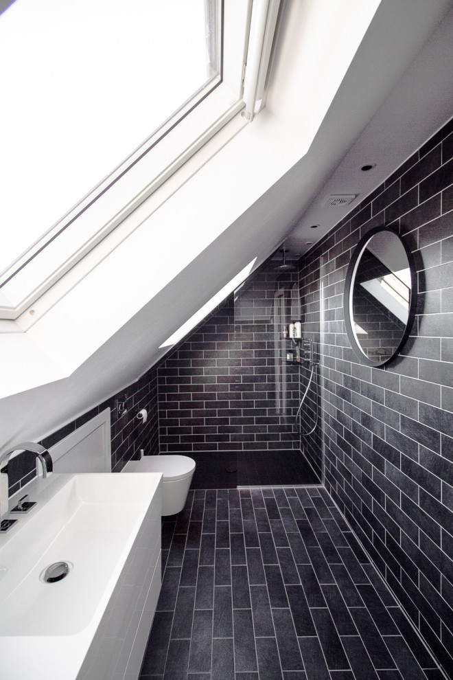 Medium sized contemporary ensuite bathroom in Surrey with raised-panel cabinets, white cabinets, a walk-in shower, a wall mounted toilet, black tiles, porcelain tiles, white walls, porcelain flooring, an integrated sink, solid surface worktops, black floors, an open shower and white worktops.