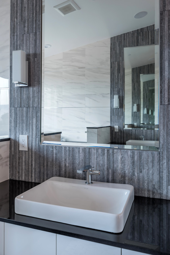 Inredning av ett modernt stort svart svart en-suite badrum, med släta luckor, vita skåp, ett fristående badkar, en öppen dusch, grå kakel, marmorkakel, grå väggar, ett fristående handfat, bänkskiva i kvarts, svart golv och med dusch som är öppen