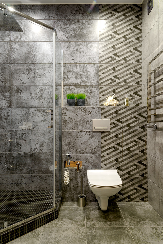 Modelo de cuarto de baño actual con ducha esquinera, sanitario de pared, baldosas y/o azulejos grises, aseo y ducha y suelo gris