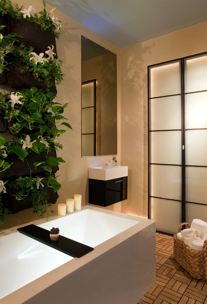 Modern inredning av ett badrum, med ett väggmonterat handfat, släta luckor, ett fristående badkar och brun kakel