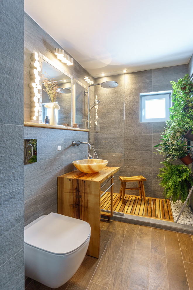 Inspiration pour une petite salle de bain ethnique avec des portes de placard blanches, WC suspendus, un carrelage gris, des carreaux de céramique, un mur gris, un sol en carrelage de céramique, une vasque et un plan de toilette en bois.