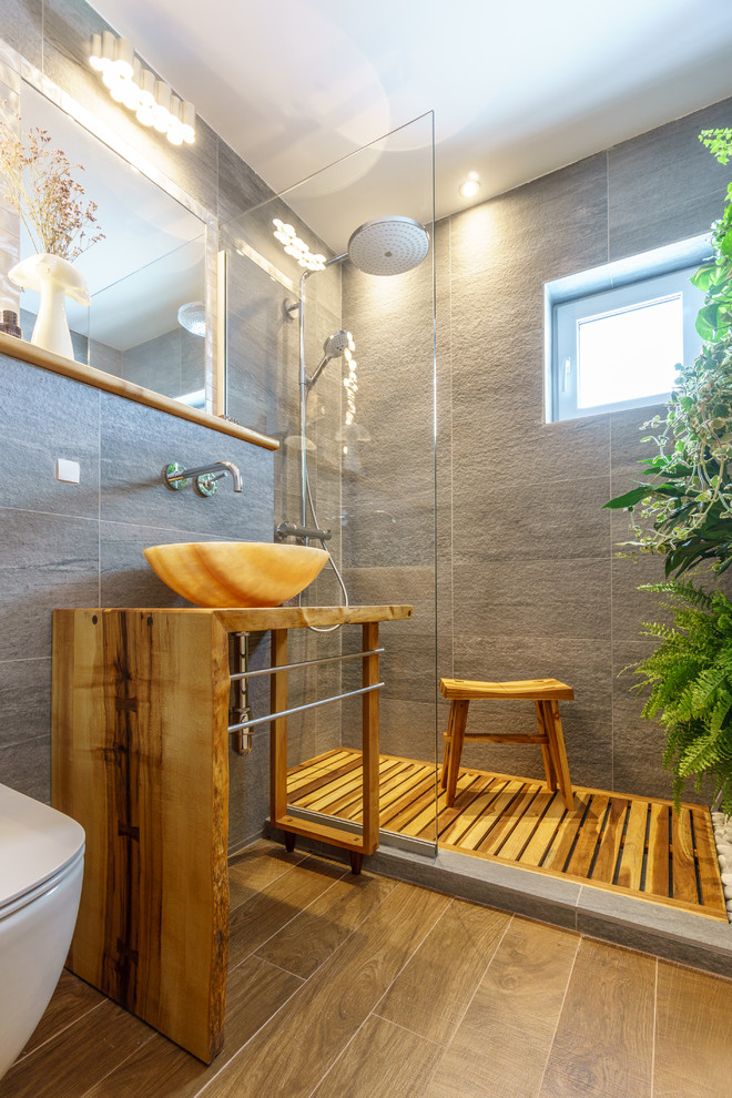 Idéer för ett litet exotiskt badrum med dusch, med vita skåp, en dusch i en alkov, en vägghängd toalettstol, grå kakel, keramikplattor, grå väggar, klinkergolv i keramik, ett fristående handfat och träbänkskiva