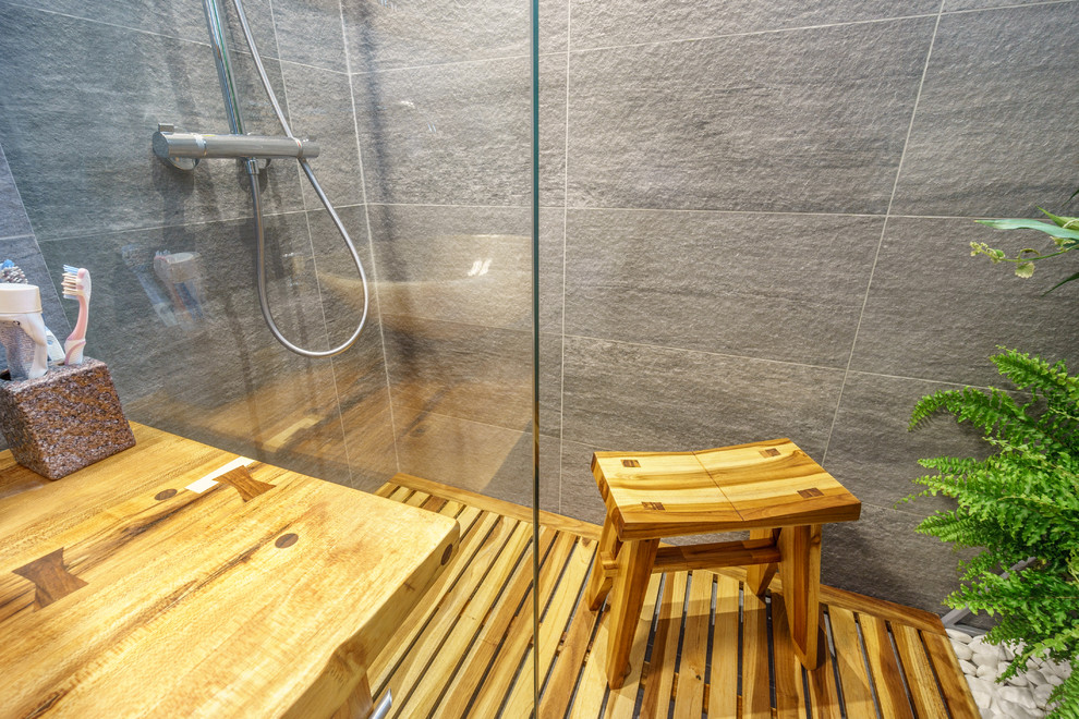 Idéer för att renovera ett litet tropiskt badrum med dusch, med vita skåp, en dusch i en alkov, en vägghängd toalettstol, grå kakel, keramikplattor, grå väggar, klinkergolv i keramik, ett fristående handfat och träbänkskiva