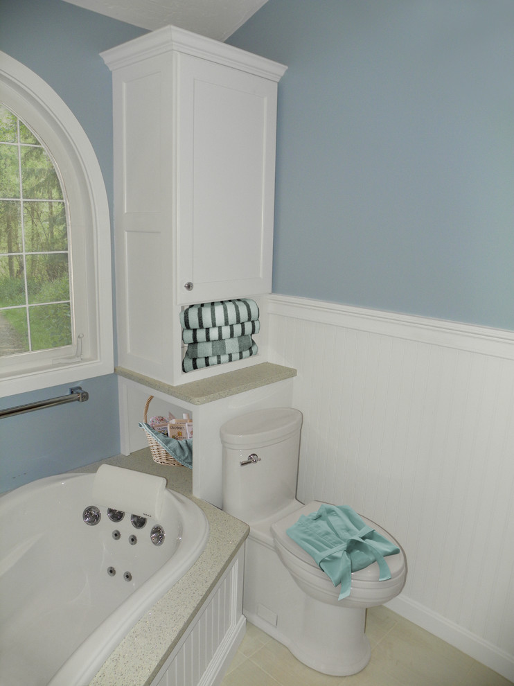 Modelo de cuarto de baño clásico de tamaño medio con aseo y ducha, lavabo bajoencimera, armarios estilo shaker, puertas de armario blancas, encimera de cuarzo compacto, jacuzzi, sanitario de una pieza, paredes azules y suelo de baldosas de porcelana