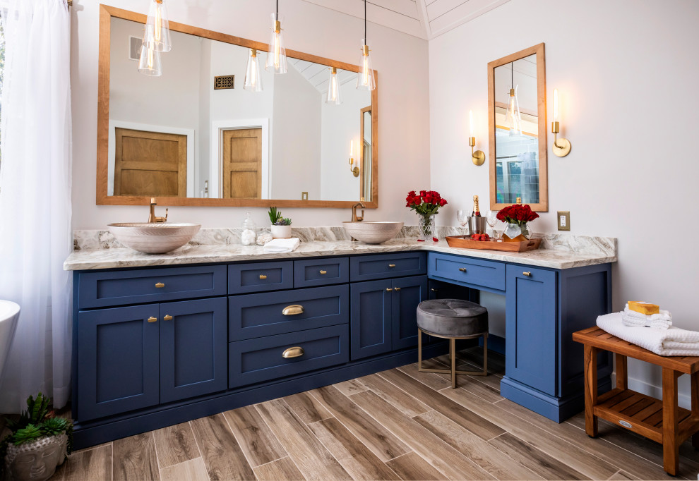 Modelo de cuarto de baño tradicional renovado con armarios estilo shaker, puertas de armario azules, bañera exenta, paredes blancas, suelo de madera en tonos medios, lavabo sobreencimera, suelo marrón y encimeras multicolor