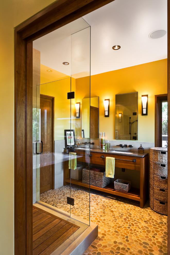 Inredning av ett asiatiskt badrum, med ett undermonterad handfat, släta luckor, skåp i mörkt trä, en dusch i en alkov, beige kakel, gula väggar, klinkergolv i småsten och beiget golv