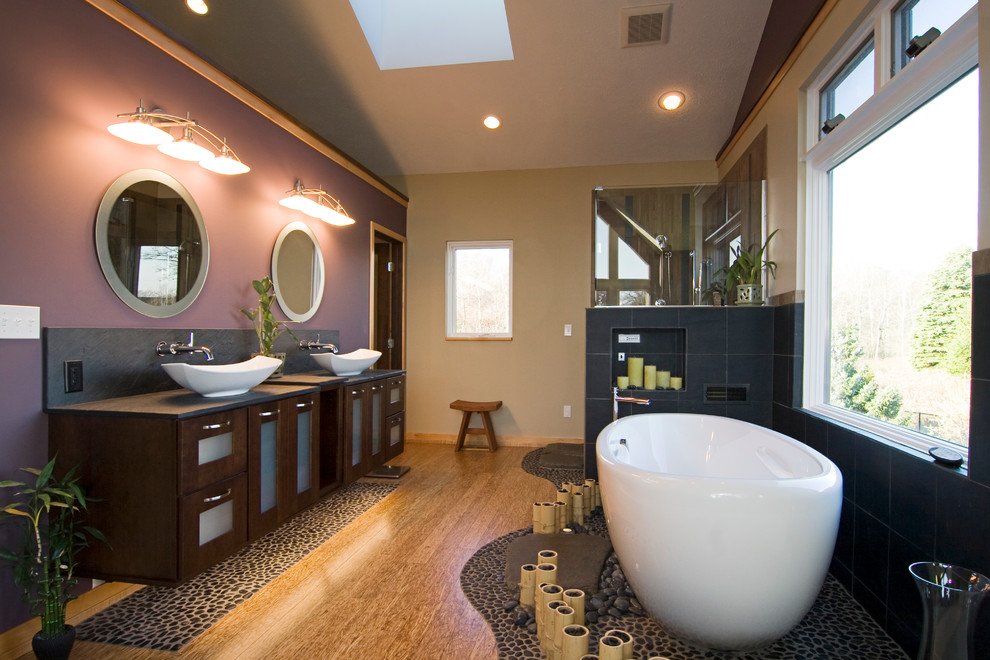 Design ideas for a large world-inspired ensuite bathroom in Grand Rapids with a vessel sink, glass-front cabinets, dark wood cabinets, a freestanding bath, a corner shower, purple walls and light hardwood flooring.
