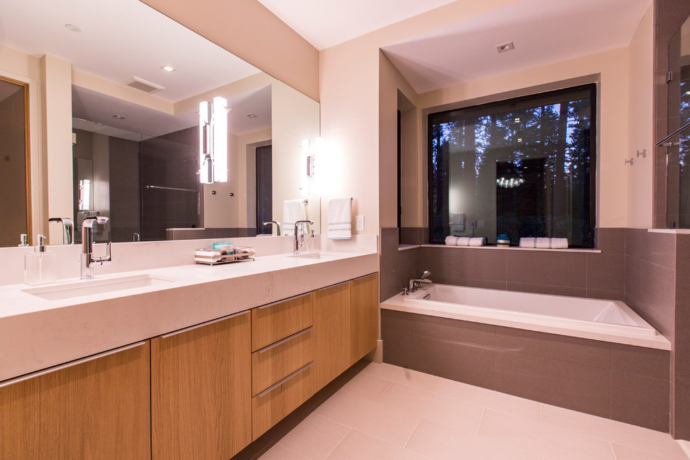 Modernes Badezimmer mit flächenbündigen Schrankfronten, hellen Holzschränken, Toilette mit Aufsatzspülkasten, braunem Holzboden, Quarzwerkstein-Waschtisch, Einbaubadewanne, Porzellanfliesen, Unterbauwaschbecken und Falttür-Duschabtrennung in Sacramento